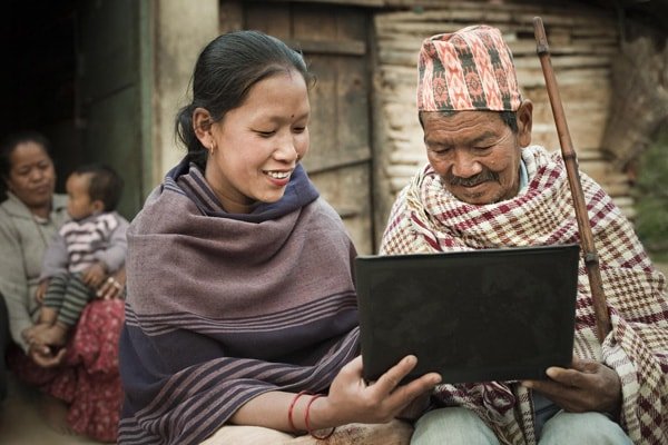 Man and woman viewing learning content on a laptop in a village setting.